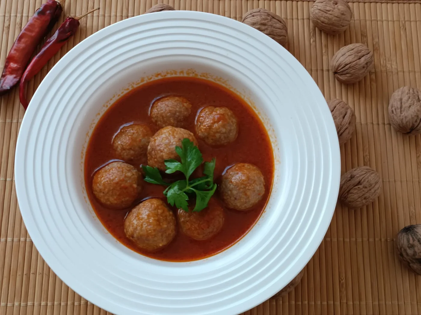 Salçalı sos içinde haşlama içli köfteler, yanında cevizler ve kuru biber